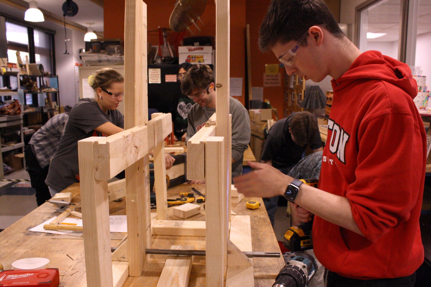 in the foreground 1 student prepares to screw part of the catapult together while the background is full of other catapult building activity