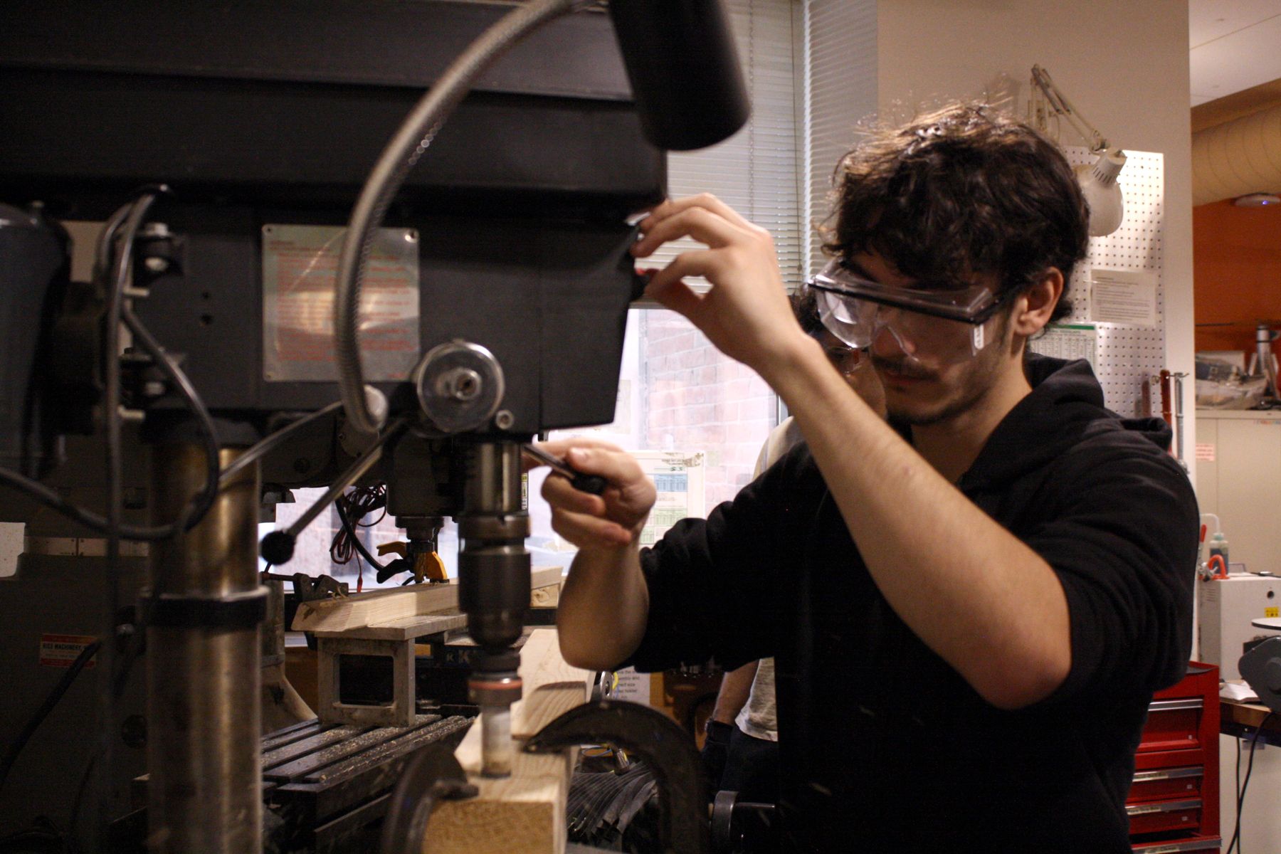 a student using the drill press to drill a larger hole into a board for his catapult