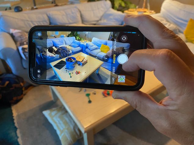 A person is using their cell phone to take a picture of a messy living room. The picture is focused on the screen of the phone.