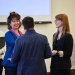 Four people engage in conversation in a conference room. Two people smile at one another in a discussion.