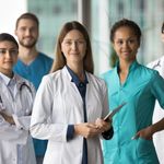 A group of doctors in white coats standing together, smiling, in a hospital corridor.