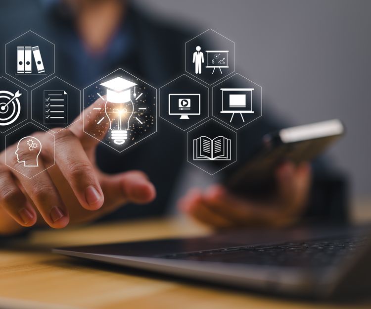 A person is touching digital icons, including a light bulb and target, in front of a laptop, suggesting innovation and technology in a business setting.