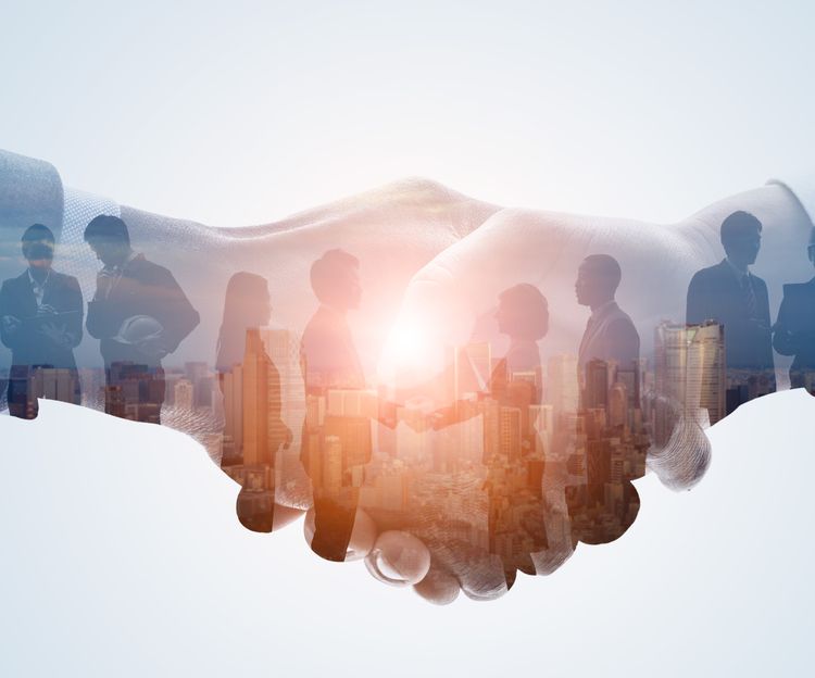 A double exposure image shows a handshake overlaying a cityscape and businesspeople silhouettes. The tone conveys collaboration and partnership.