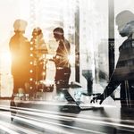 A blended image showing silhouettes of business people working on laptops overlaid with a cityscape and blurred lights, conveying a sense of dynamic teamwork and urban life.