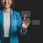 A woman in a blue blazer interacts with a virtual touch interface, smiling confidently. Transparent rectangular icons float in front of a dark background.