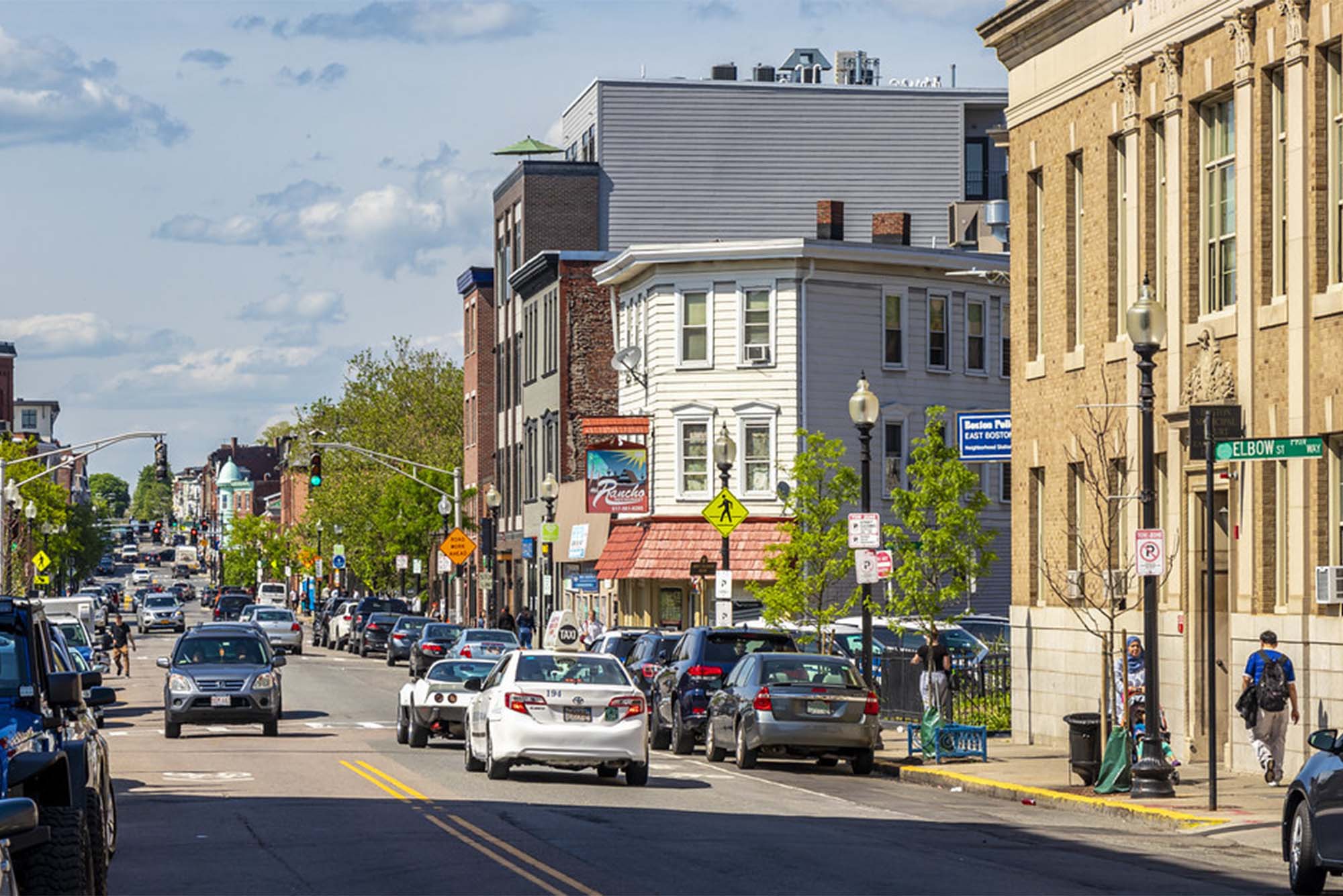 Meridian Street in East Boston, busy with cars, bikes and pedestrians on a sunny day. Photo by Brandon Bartoszek