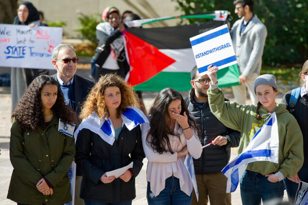 Lucy Anisimov (CAS'19) (center, in white), who is from Israel, becomes emotional during a vigil for victims of terrorism in Israel sponsored by BU Students for Israel on October 16 in Marsh Plaza. In the background, BU students hold Palestinian flags and signs reading "Resistance Does Not Equal Terrorism" and "BU Mourns All Lives Lost to State Terrorism." Photo by Cydney Scott