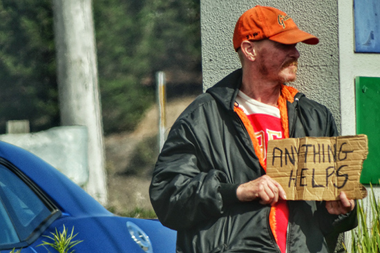 man holding a sign that says "anything helps" begs for money on the streets