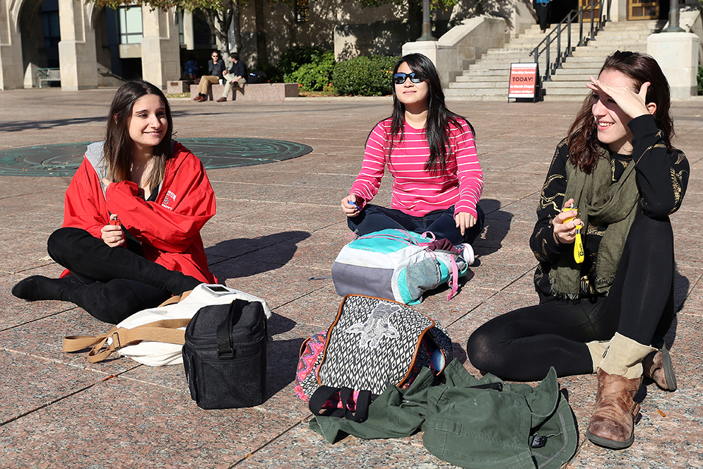 Emma Zampino (CAS ’16), left, Irene Hsueh (CAS ’16) and Kim Kaelin (CAS ’16), right, sit on Marsh Plaza to observe people for a experimental psychology class assignment. Zampino keeps count of the total number of people walking by the plaza. Hsueh and Kaelin use their trackers to record how many of those people are texting or actively using their cellphones while walking.