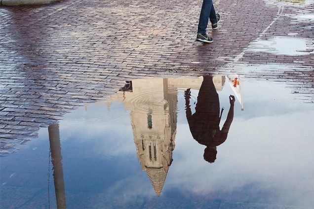 a puddle reflects the a pedestrian passerby and building on the Boston University Charles River campus