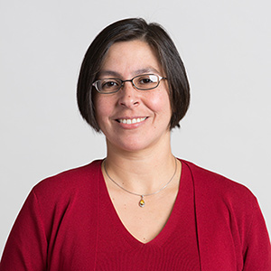 Photo: Headshot of Tammy Vigil. A white woman with short brown hair and wearing glasses and a red blouse smiles and poses for the camera.