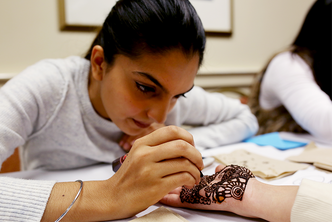 A student paints henna on another student's hand during the Chand Raat celebration at Boston University