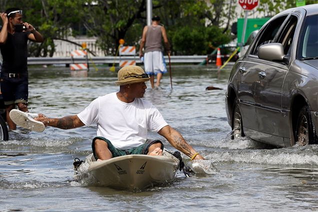 Juan Carlos Sanchez uses his shoes to paddle a kayak on a flooded street near Collins Ave.