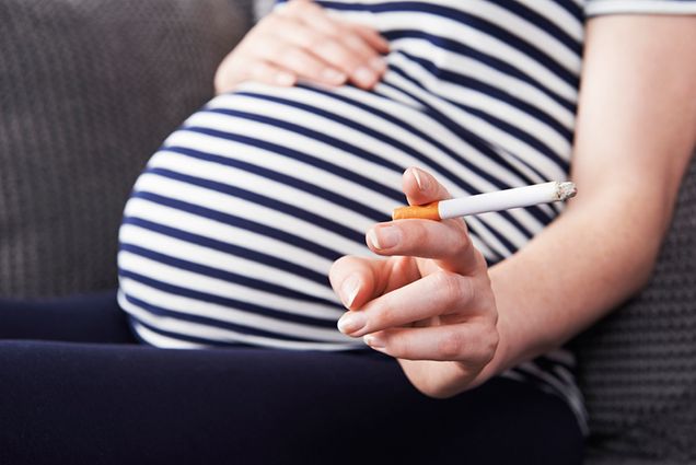 Photo of a pregnant mother holding her stomach and smoking