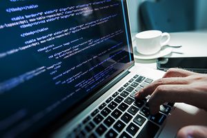 Laptop open with coding on the screen and a man's hand on the keyboard