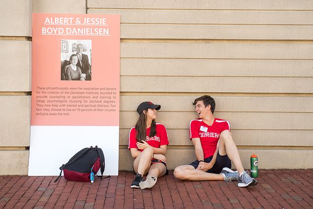 Juliet Stein and Zachary Prescott lean against wall next to poster