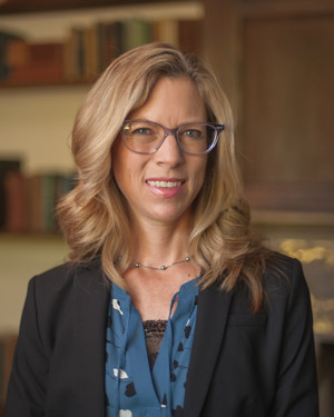 Photo: Headshot of a woman with light hair and glasses smiling