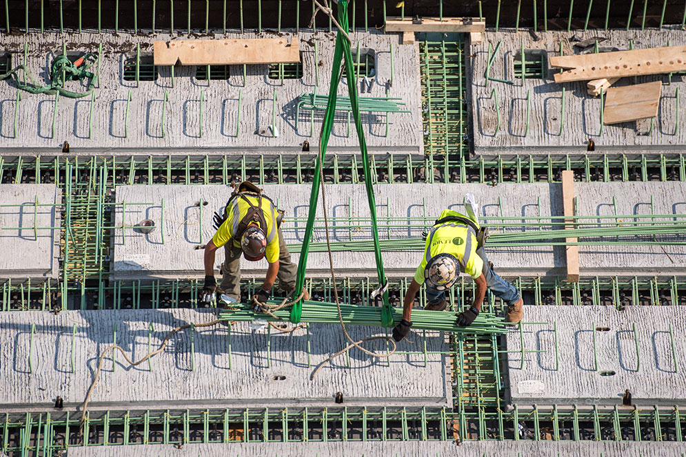 two construction workers balance on a sea of green pegs