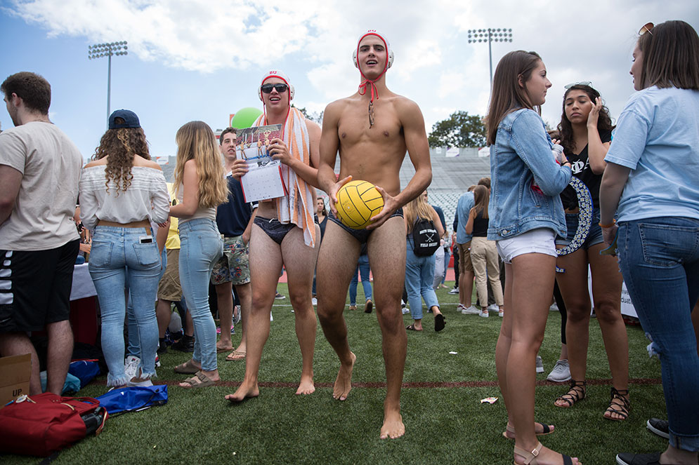 Two students on Nickerson field in their water polo uniforms holding their signature water polo team calendar