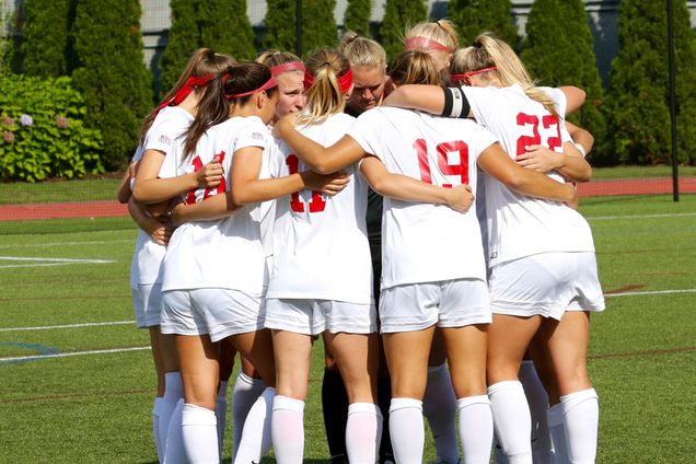 BU Terriers women's soccer team comes together in a huddle on the field.