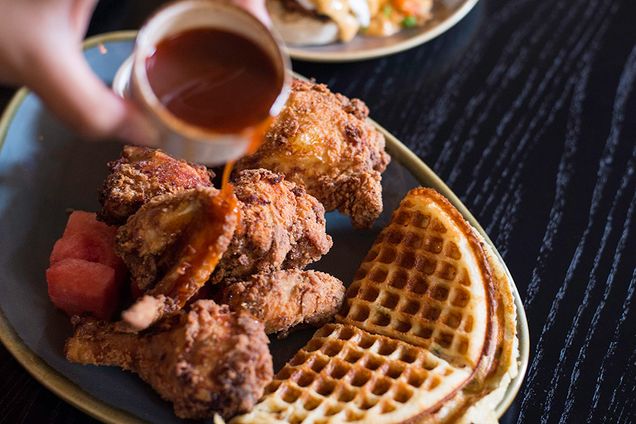 A person pours maple syrup on chicken and waffles at Buttlermilk & Bourbon restaurant in Boston