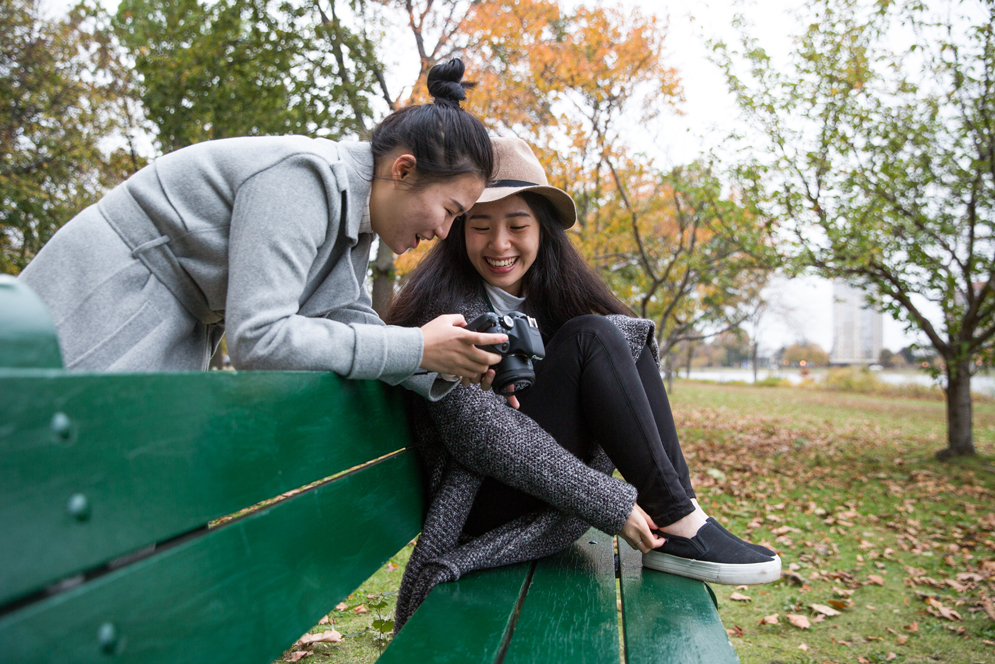 Two students look at photographs on a camera during a photoshoot on the Esplanade. 