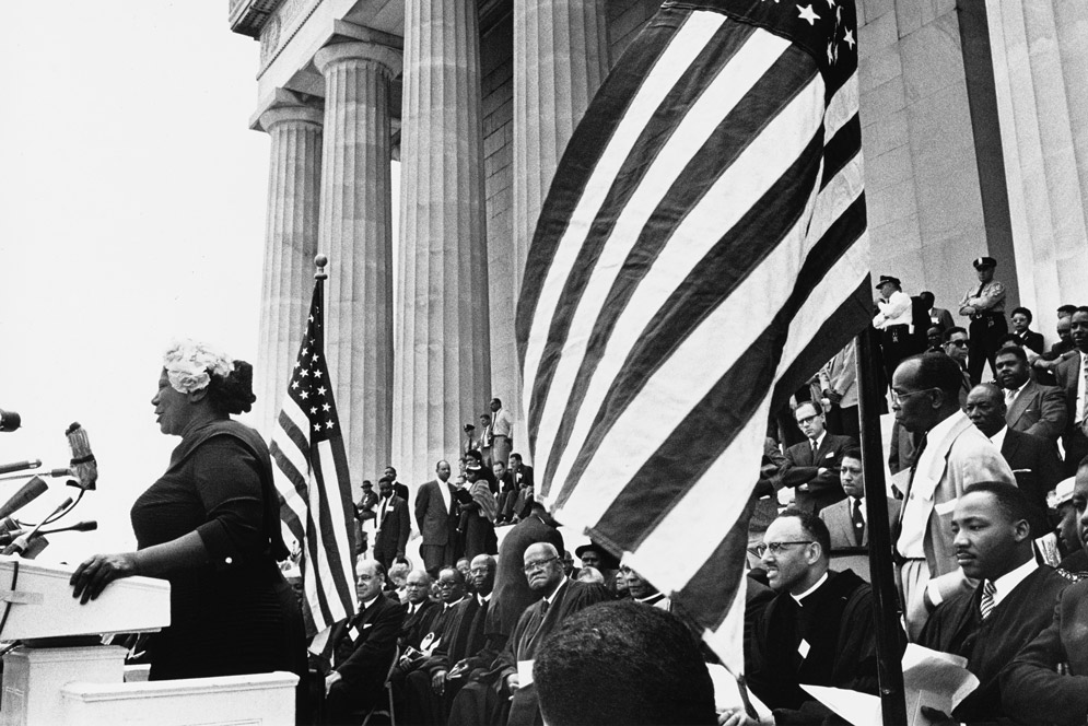 Mahalia Jackson speaks at podium alongside Dr. Martin Luther King Jr.