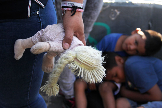 A Mexican woman holds a doll next to children at the Paso Del Norte Port of Entry, in the US-Mexico border in Chihuahua state, Mexico on June 20, 2018