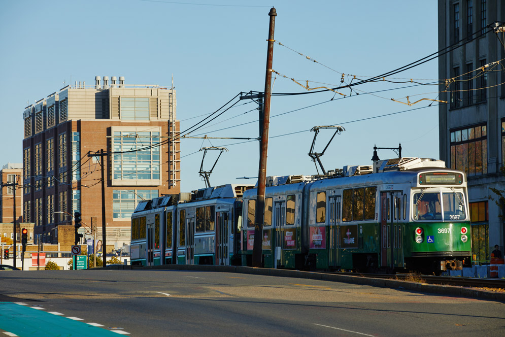 Photo: The MBTA Green B Line moves down the track o Commonwealth Ave. as the sun sets. Red brick Boston University buildings can be seen in the background.