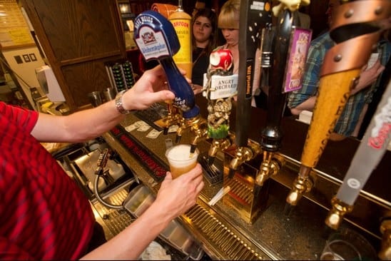 A bar tender pours beer from tap handles