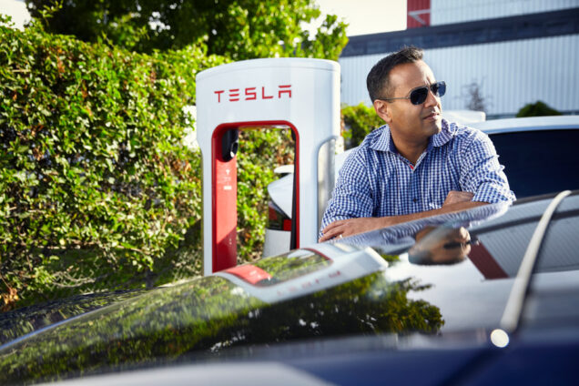 Alum Parag Vaish rests his arms on a Tesla