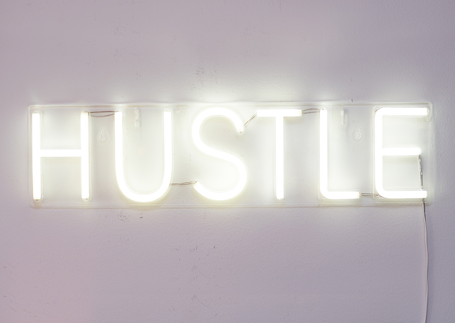 A neon sign that says 'HUSTLE' hanging on a wall.