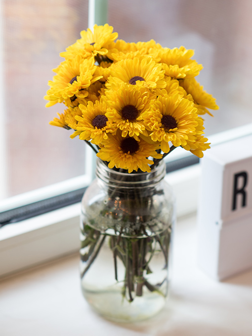 A bunch of sunflowers in a mason jar rest on a white windowsill.