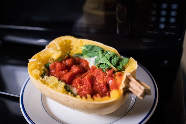 A microwaved stuffed spaghetti squash on a plate in front of a microwave.