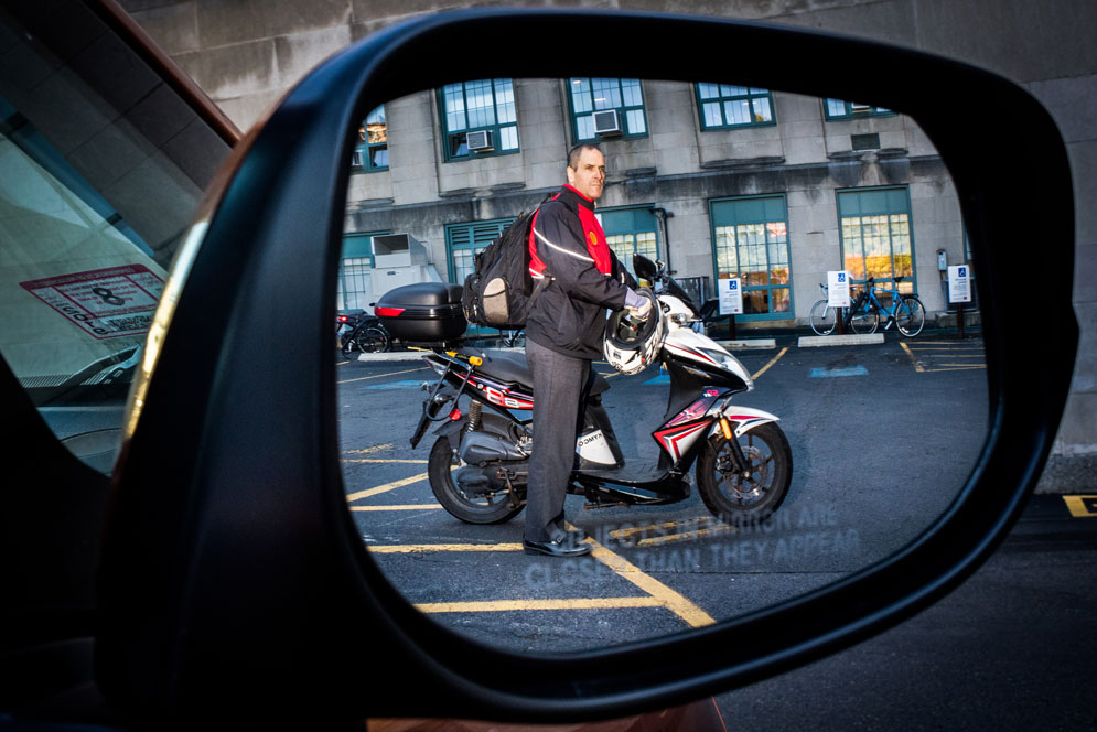 Man standing with his motorbike pictured in a rear view mirror