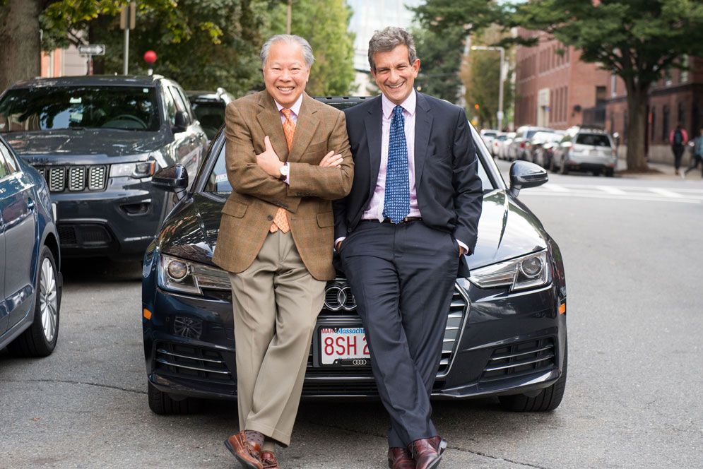 Two faculty members standing in front of the Audi they carpool in