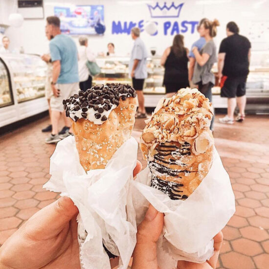two people hold cannoli at Mike's pastry