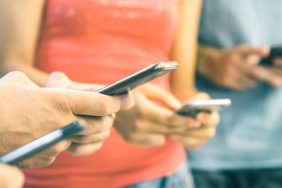 Photo: Shot of various people looking at their smartphones. Photo is zoomed in so only torsos and hands are shown.