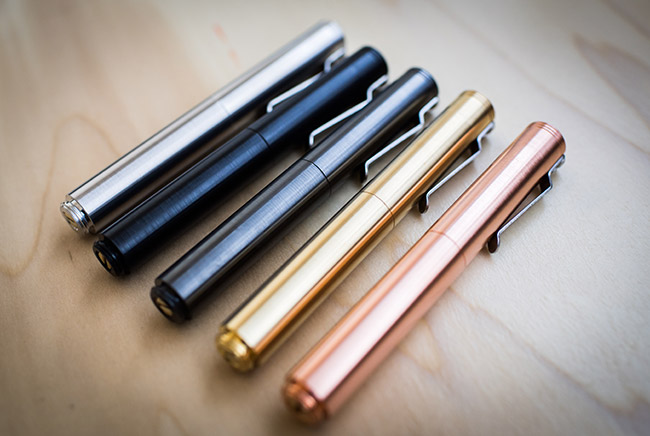 Detail photo of aluminum pens made by Schon DSGN in multiple colors lying on a wooden table.