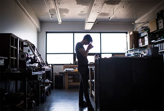 Schon Horology founder Ian Schon, silhouetted against sunlight coming through the windows, works in his Allston, MA studio.