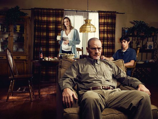 Breaking Bad character Walter White sits in a recliner with his family wife Skylar and son Walt Jr. in the background.