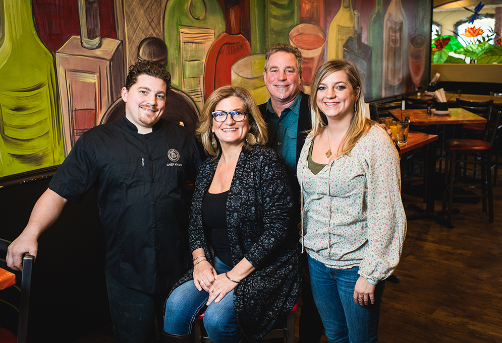 Portrait of Flying Rhino owners Paul and Melina Barber with children Tory and Myles Barber standing in The Flying Rhino Cafe & Watering Hole in Worcester, Massachusetts