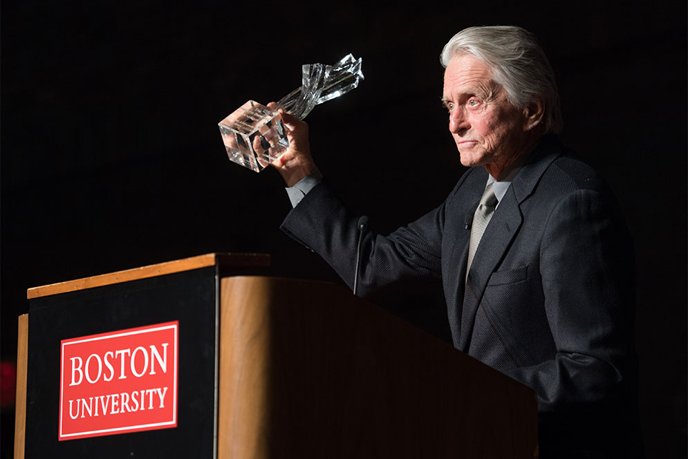 Michael Douglas holds up his Bette Davis Lifetime Achievement Award trophy at the podium after giving a reception speech.