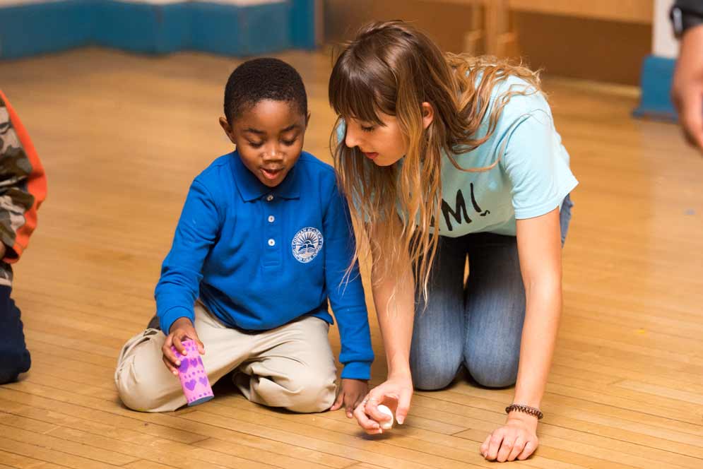 A student kneels next to a five-year-old and talks with him