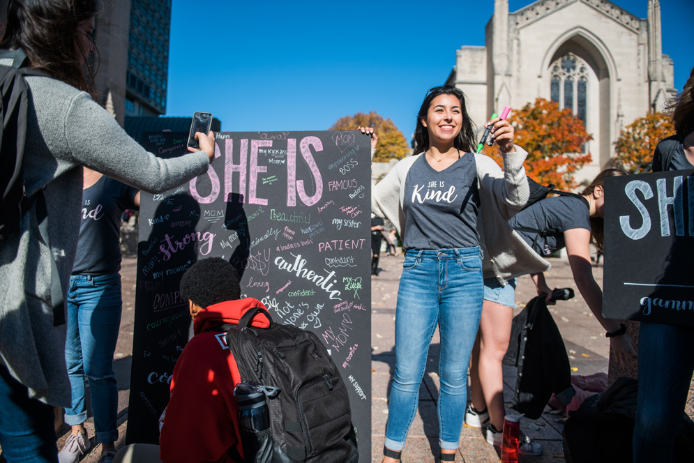 Students write the names of women who have inspired them down on a sign in colorful paint