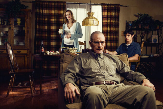 Breaking Bad character Walter White sits in a recliner with his family wife Skylar and son Walt Jr. in the background.