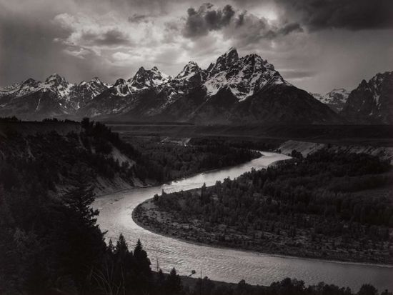 a black and white photograph of a mountain and river
