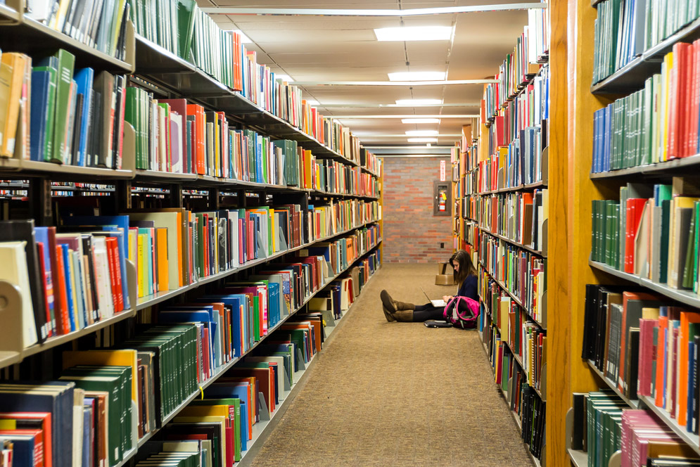 A student studies among the bookcases in Mugar Library