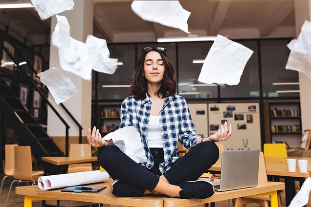 A student meditates on a table while school papers fly around her.