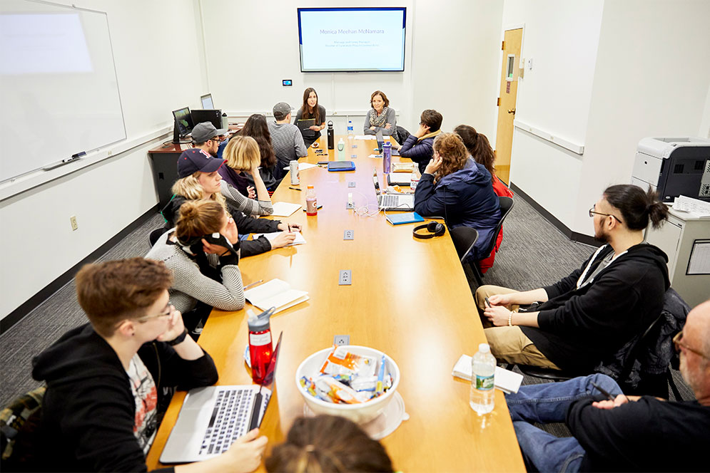 Students sit around a long table in a Trauma Journalism class.